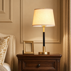 Gold and black table lamp with a glowing fabric shade on a wooden bedside table.
