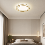 Gold circular ceiling light glowing above a modern bedroom with a matching pendant lamp.