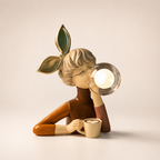 Stylized woman figurine with leaf headband blowing a glass bubble while holding a mug.