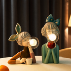Two decorative girl figurine lamps with glowing glass globes sit on a table.