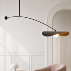 Modern mobile pendant light with curved black arm, sculptural brown blades, and a glowing bulb in a white room.