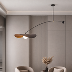 Modern black arc pendant lamp with petal shades and glowing bulb above a neutral living room wall.