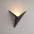 Black triangular wall sconce casting a warm upward glow on a pale textured wall.