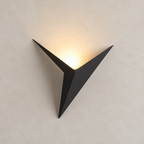 Black angular wall sconce with warm light glowing upward on a pale wall.