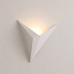 White angular wall sconce glowing warmly on a pale minimalist wall.