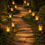 Black solar torch path lights with glowing flame bulbs lining a garden walkway at night.