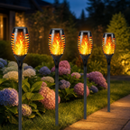 Four black solar torch garden lights glow with flame effects among flowers and grass.