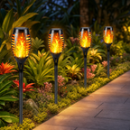 Four black solar flame lamps glow along a garden path.