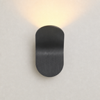 Black rounded wall sconce casting a warm upward glow on a pale wall.