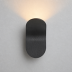 Black rounded wall sconce casting a warm glow on a pale wall.
