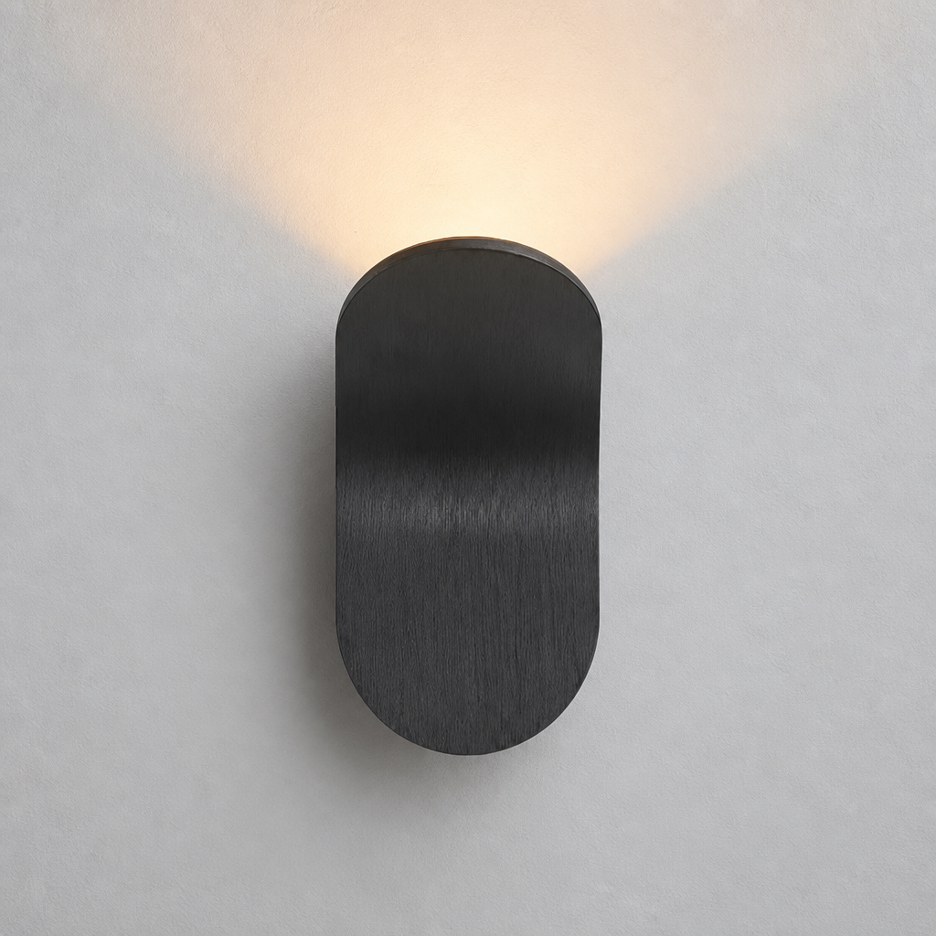 Black rounded wall sconce casting a warm glow on a pale wall.
