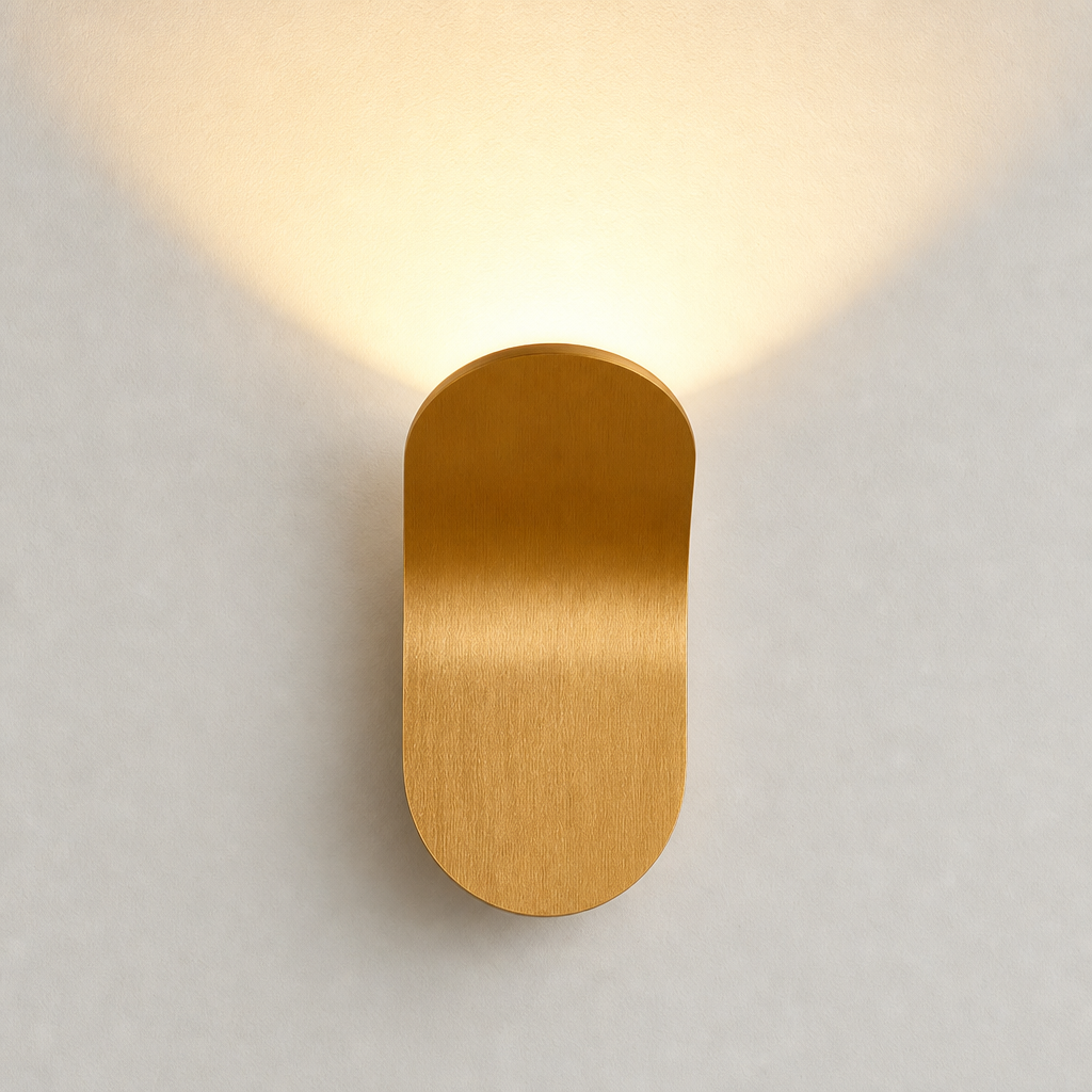 Gold capsule wall sconce with warm upward glow on a pale wall.