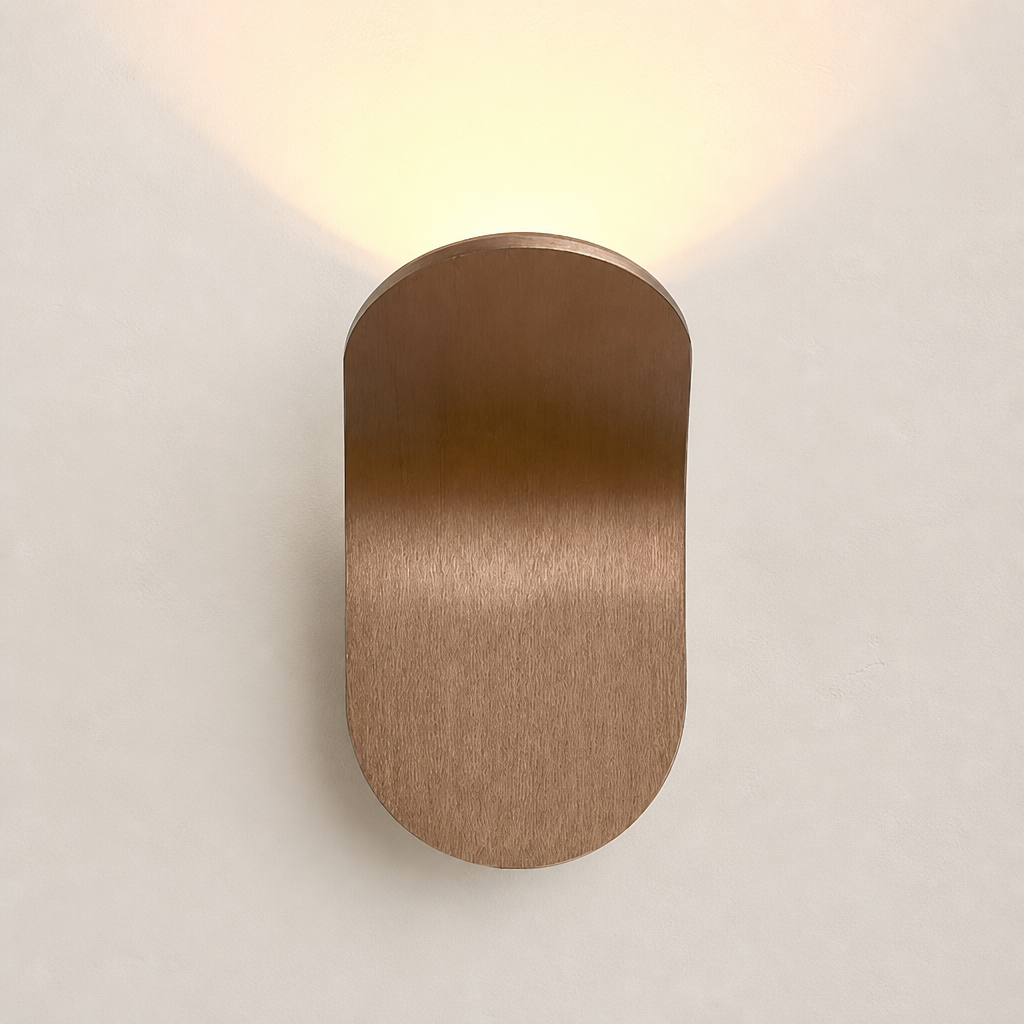 Brushed bronze rounded wall sconce casting a warm glow on a pale wall.