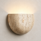 Beige semicircular stone wall sconce glowing softly on a pale textured wall.