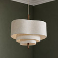 Tiered cream fabric pendant light with warm wood stem hanging in a green room.