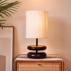Warm table lamp with a white ribbed shade and dark rounded base on a wooden cane-front nightstand.