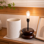 Glowing Edison bulb lamp with dark round base beside a white ribbed cylindrical shade.
