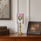 Pink rose stained-glass table lamp with ornate brass base on a wooden cabinet.