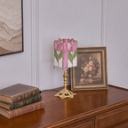 Pink tulip stained-glass table lamp with an ornate gold base on a wooden dresser.