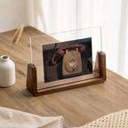 Clear acrylic photo frame with wooden base displaying a vintage rotary phone on a wooden desk.