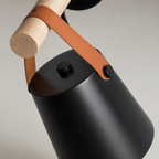 Matte black cylindrical kettle with a tan leather strap and pale wooden handle.