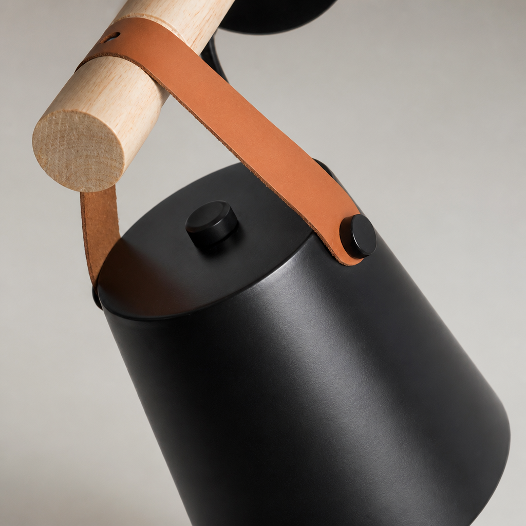 Matte black cylindrical kettle with a tan leather strap and pale wooden handle.