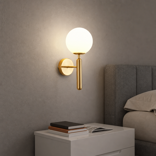 Gold wall sconce with glowing white globe above a white bedside table near a gray upholstered bed.