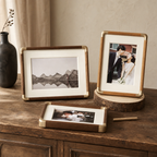 Three wood-and-brass photo frames with ivory mats displayed on a rustic wooden cabinet.
