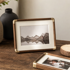 Wood and brass photo frame with white mat displaying a mountain landscape on a rustic table.
