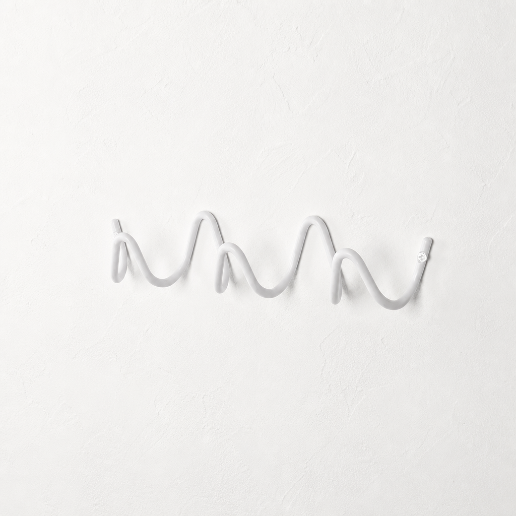 White wavy wall-mounted hook rail on a plain white textured wall.