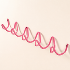 Pink wavy wall-mounted metal rack with screw holes on a plain white background.