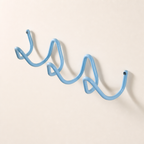 Light blue wavy wall-mounted hook rack with screw caps on a plain wall.