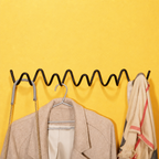 Black wavy wall coat rack holding a beige coat, purse strap, and cream scarf on a yellow wall.