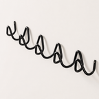 Black wavy metal wall rack with multiple curved hooks on a plain light wall.
