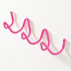 Pink wavy wall-mounted hook rack with screw ends on a white wall.