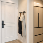 Black wavy wall hook rack holding tote bags beside a white door.