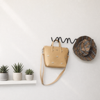 Black wavy wall hook rack holding a beige handbag and plaid hat above small potted plants.