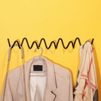 Black wavy wall rack holding a beige coat, chain strap, and cream scarf on a yellow wall.