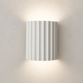 White ribbed cylindrical wall sconce glowing warmly on a plain wall