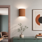 Fluted wooden wall sconce above a green console with a small potted plant.