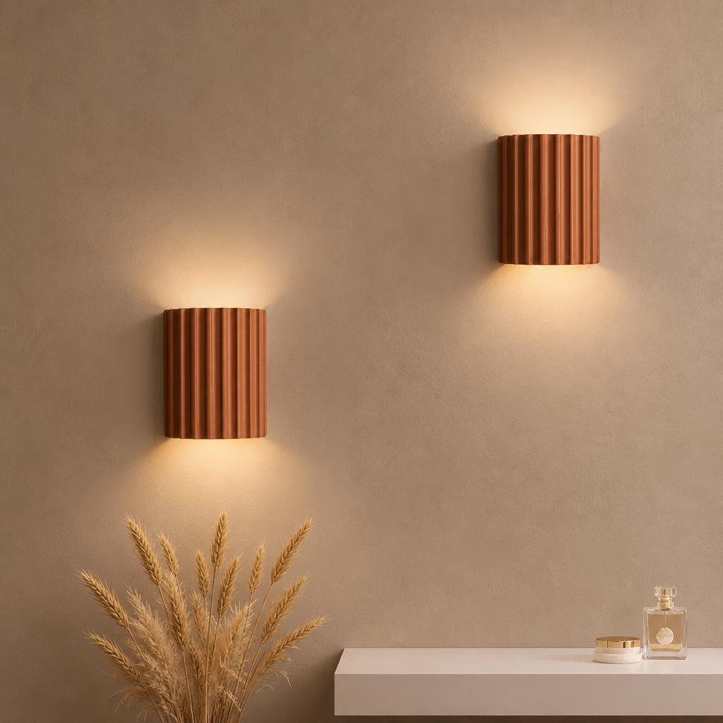 Two ribbed terracotta wall sconces glowing warmly above a white console with dried wheat.