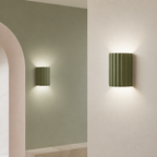 Two olive green ribbed cylindrical wall sconces casting soft up-and-down light.