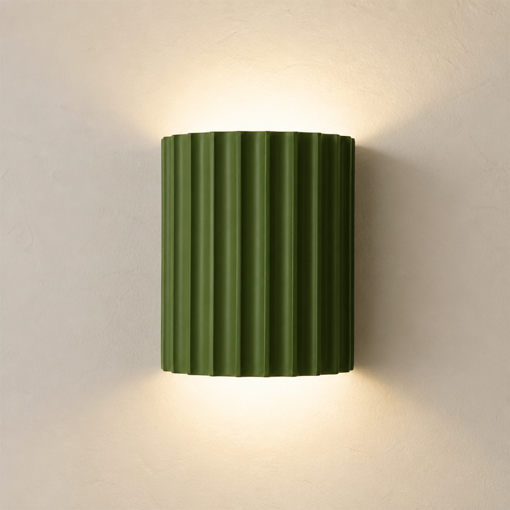 Olive green ribbed wall sconce glowing softly on a plain light wall.