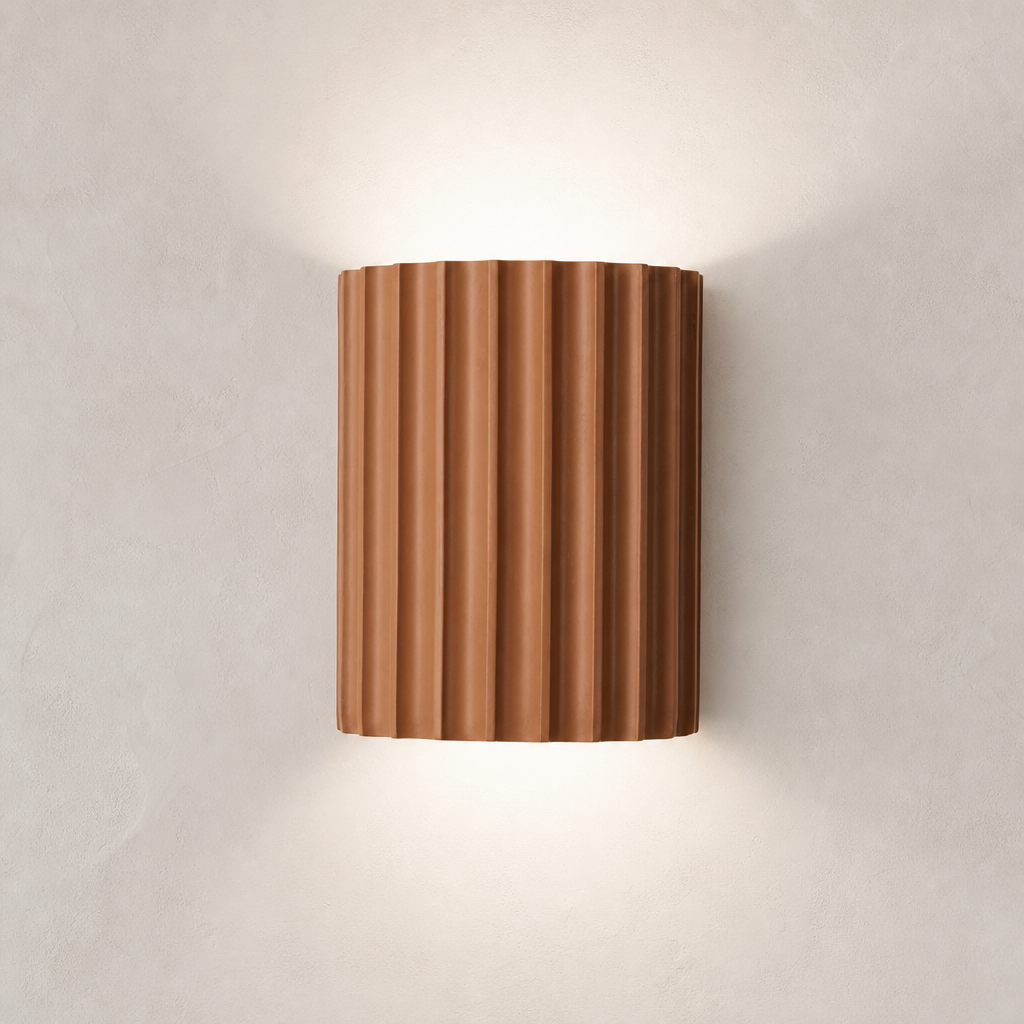 Ribbed terracotta cylindrical wall sconce casting soft light on a neutral wall.
