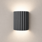 Dark ribbed cylindrical wall sconce emitting warm light above and below.