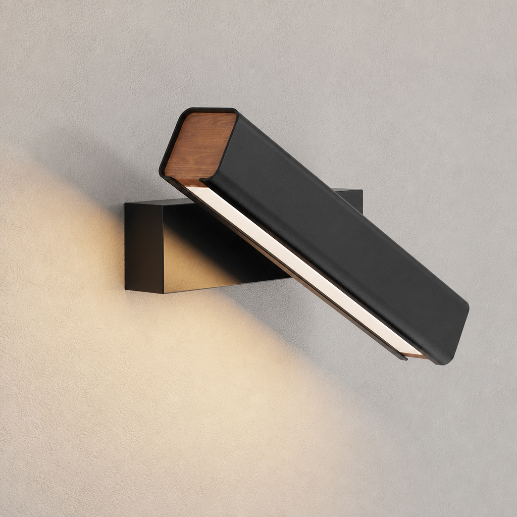 Black wall-mounted linear lamp with wood ends casting warm light on a textured wall.