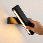 Hand adjusting a black wall-mounted linear sconce with warm LED light.