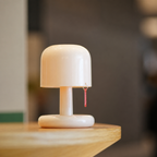 Glossy cream mushroom-shaped table lamp with a small red pull tag on a wooden tabletop.