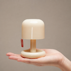 Cream mushroom-shaped mini lamp with red tag resting on an open hand.