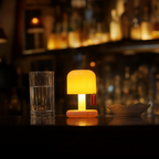 Glowing mushroom-shaped table lamp on a bar counter beside a tall glass and small dish.